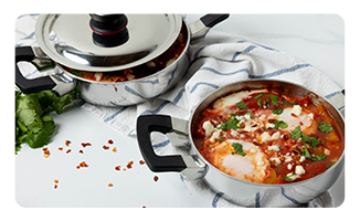 Two Royal Prestige casseroles filled with pozole ingredients near a towel and bunch of cilantro.