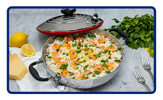 A Royal Prestige paellera filled with paella and surrounded by forks, cilantro and lemons.