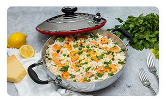 A Royal Prestige paellera filled with paella and surrounded by forks, cilantro and lemons.